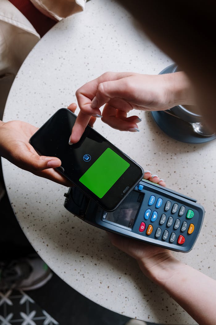 A close-up of a smartphone making a contactless payment on a terminal in a cafe setting.